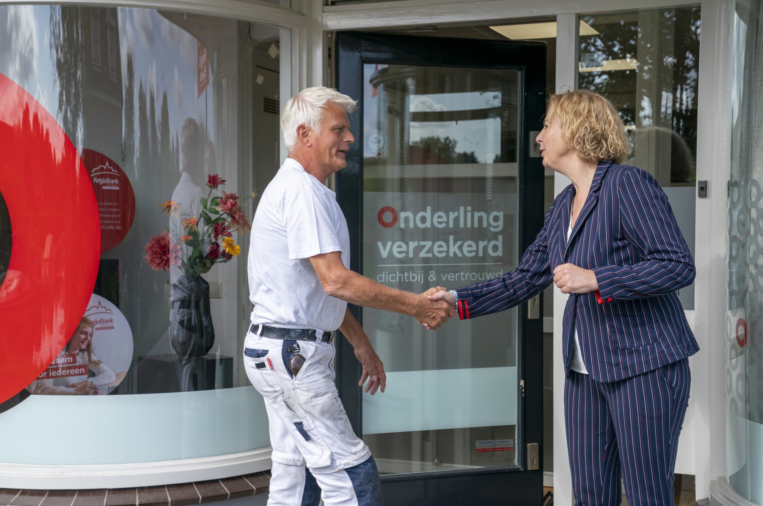 Klantadviseur schud klant de hand bij de voordeur van Onderling Verzekerd. Klantadviseur schud klant de hand bij de voordeur van Onderling Verzekerd.